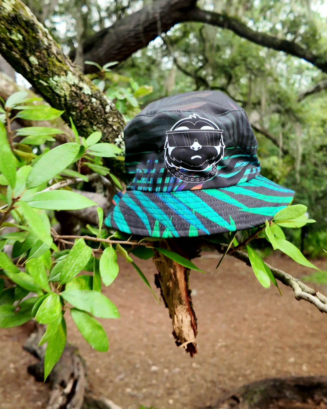 SLOTH reversible bucket hat, jungle side, hanging on a tree branch in the forest