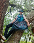 Person sitting in a tree wearing the SLOTH Jungle Pashmina over their shoulders with the SLOTH reversible bucket hat
